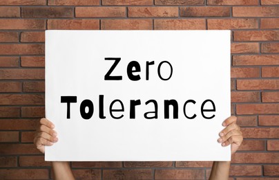 Image of Man holding poster with words Zero Tolerance near red brick wall, closeup