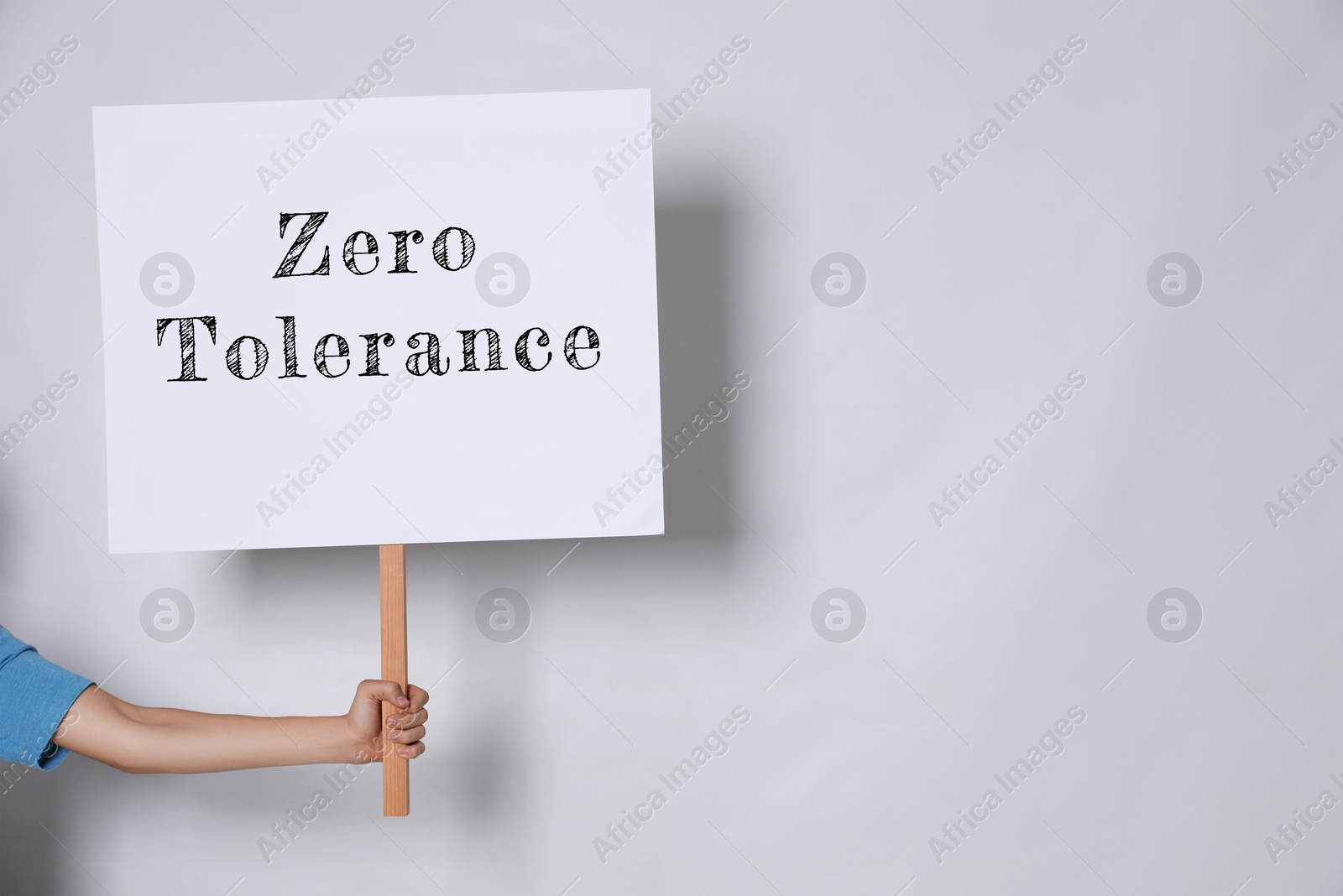 Image of Woman holding sign with words Zero Tolerance on light grey background, closeup. Space for text