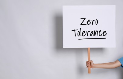 Image of Woman holding sign with words Zero Tolerance on light grey background, closeup. Space for text