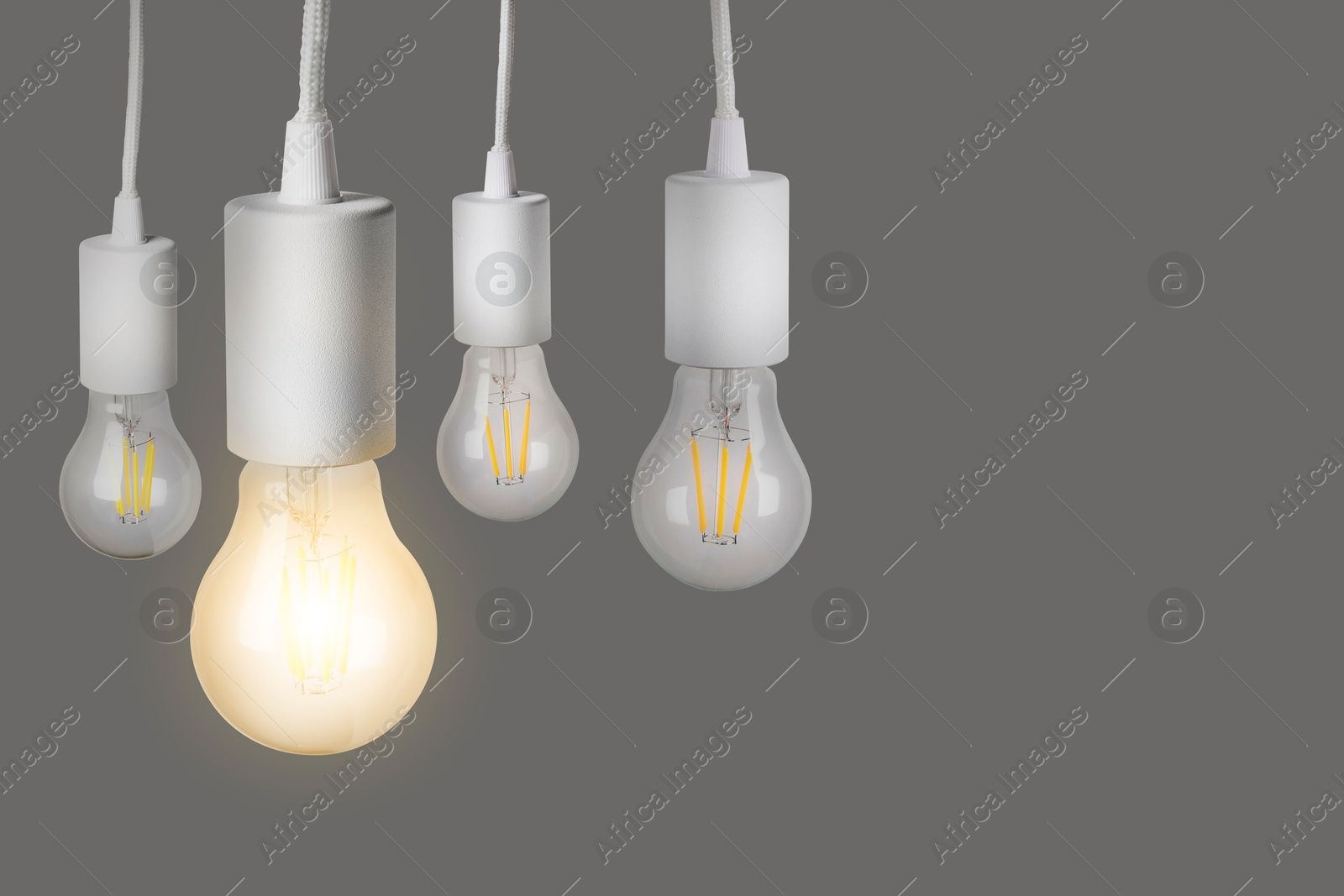 Image of One glowing light bulb among others on grey background