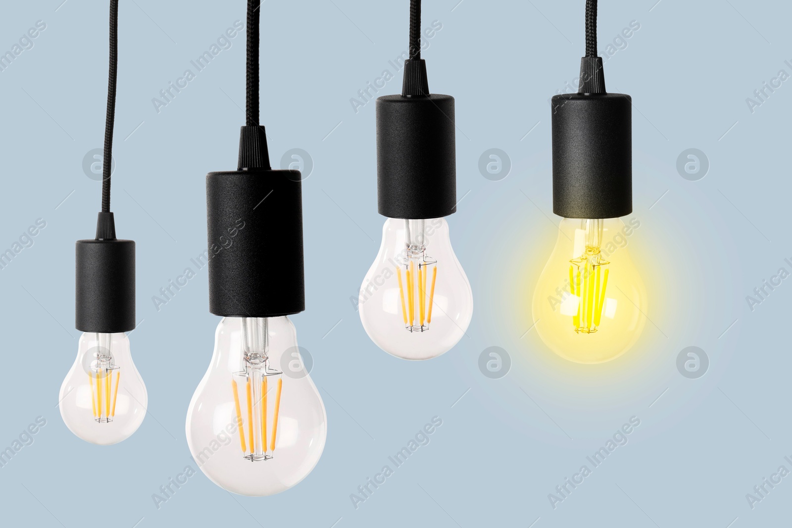 Image of One glowing light bulb among others on light blue background