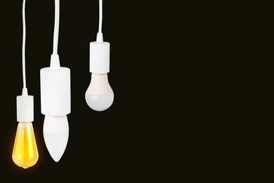 Image of Different light bulbs hanging on black background. Space for text