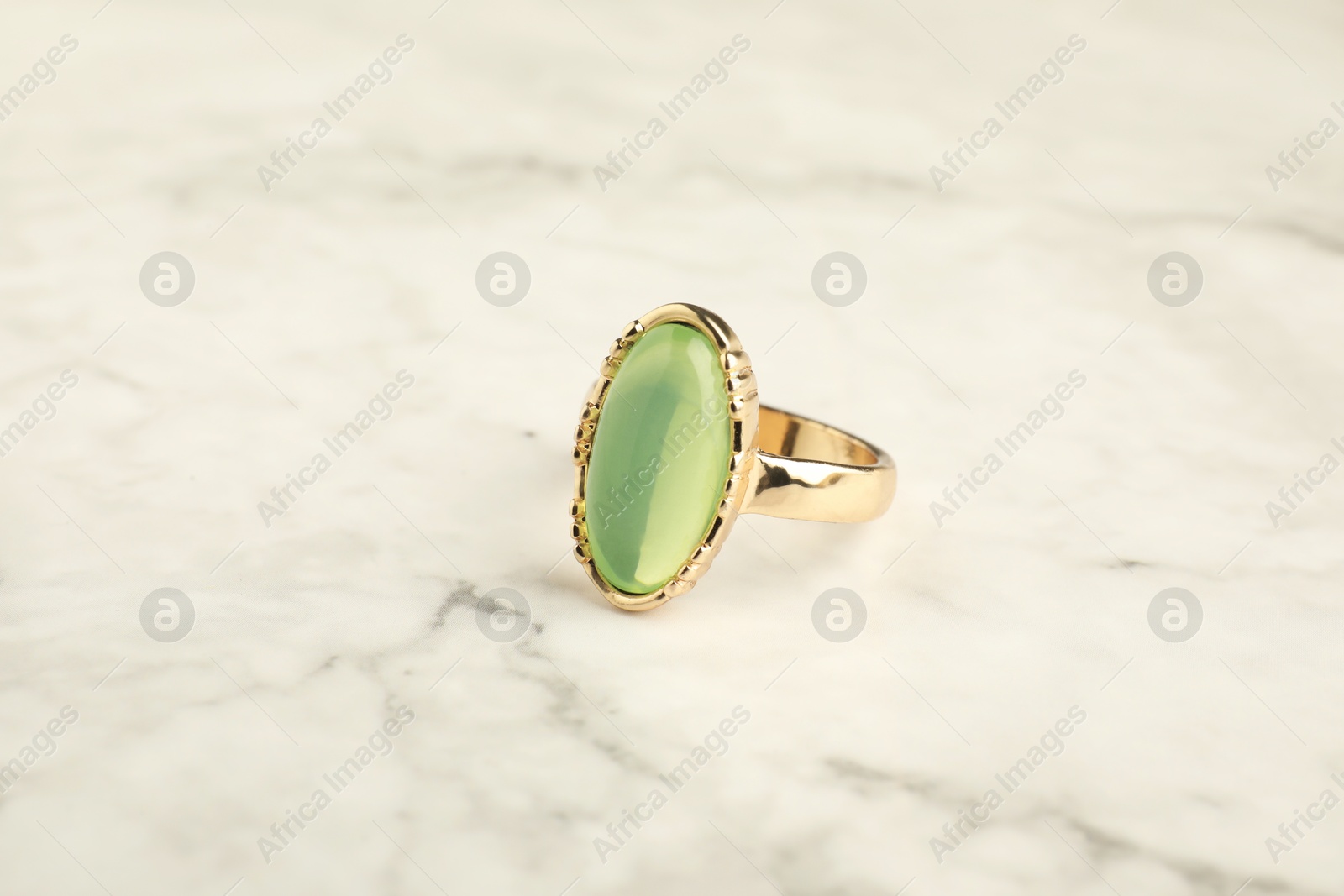 Photo of Beautiful bijouterie. Stylish ring on white marble table, closeup