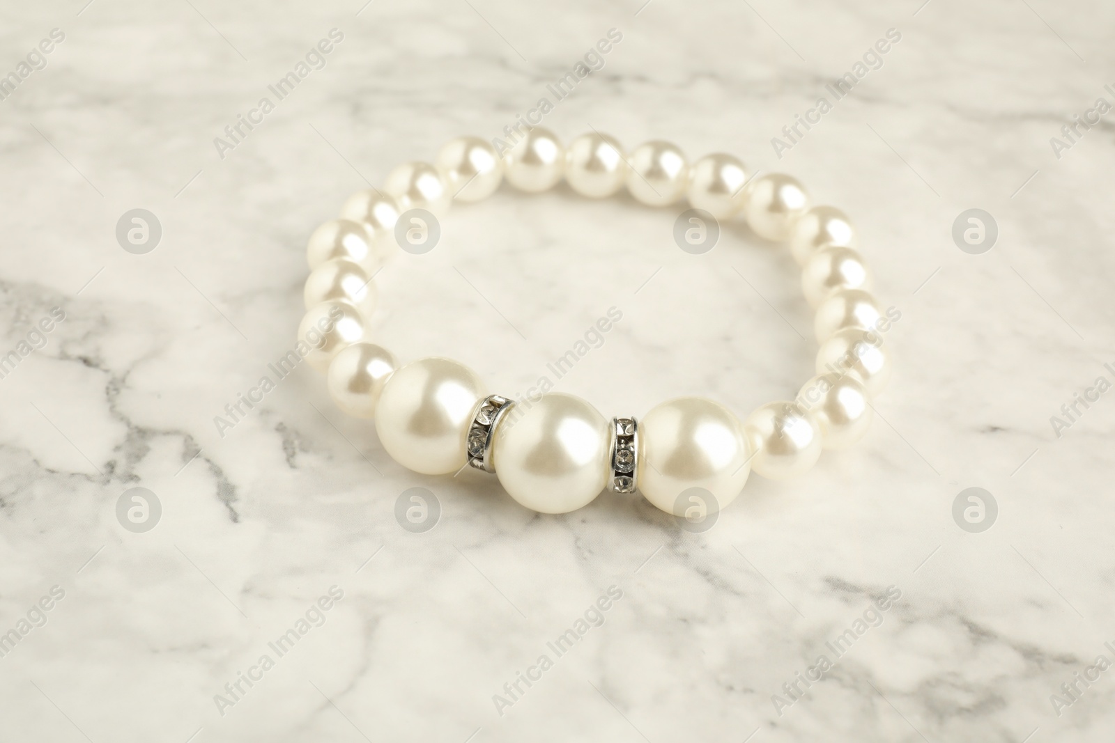 Photo of Beautiful bijouterie. Stylish bracelet on white marble table, closeup