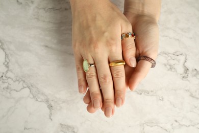 Beautiful bijouterie. Woman wearing different stylish rings at white marble table, top view