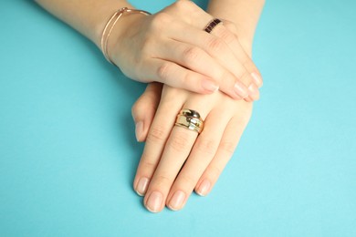 Beautiful bijouterie. Woman wearing stylish rings on and bracelet light blue background, closeup