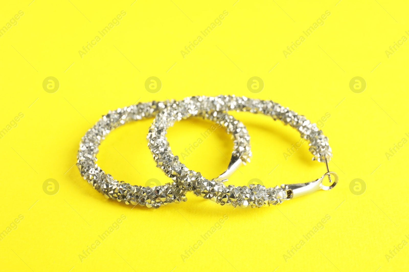 Photo of Beautiful bijouterie. Stylish earrings on yellow background, closeup