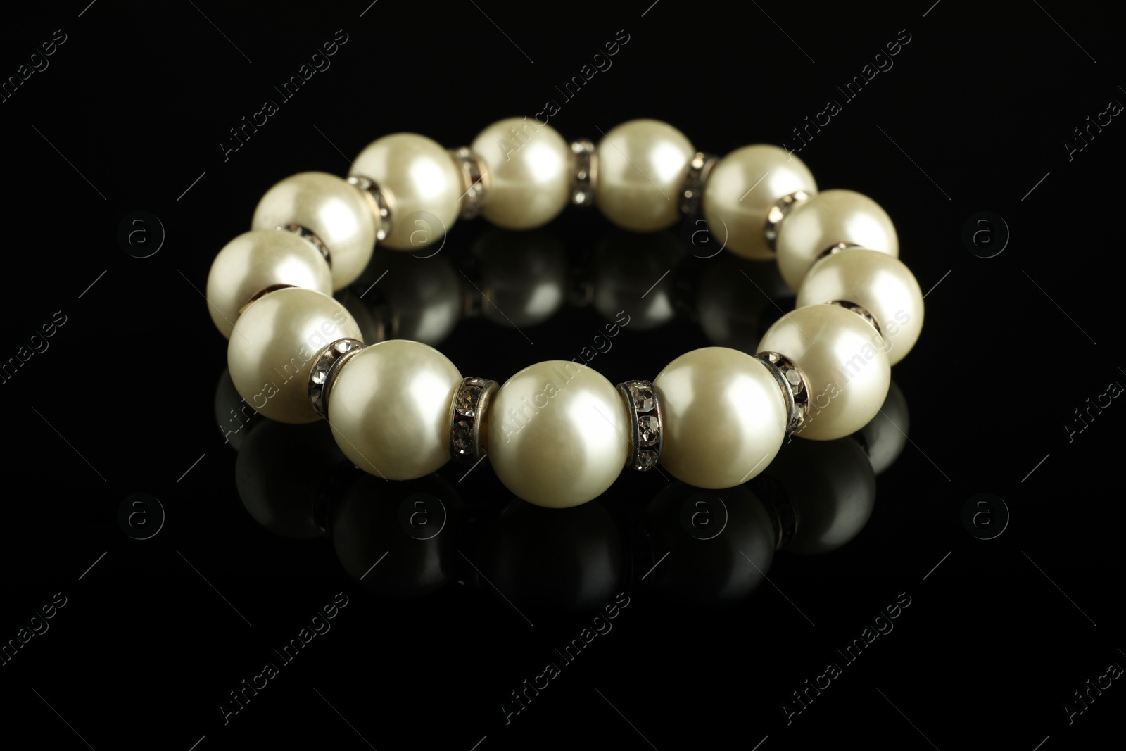 Photo of Beautiful bijouterie. Elegant bracelet on black mirror surface, closeup