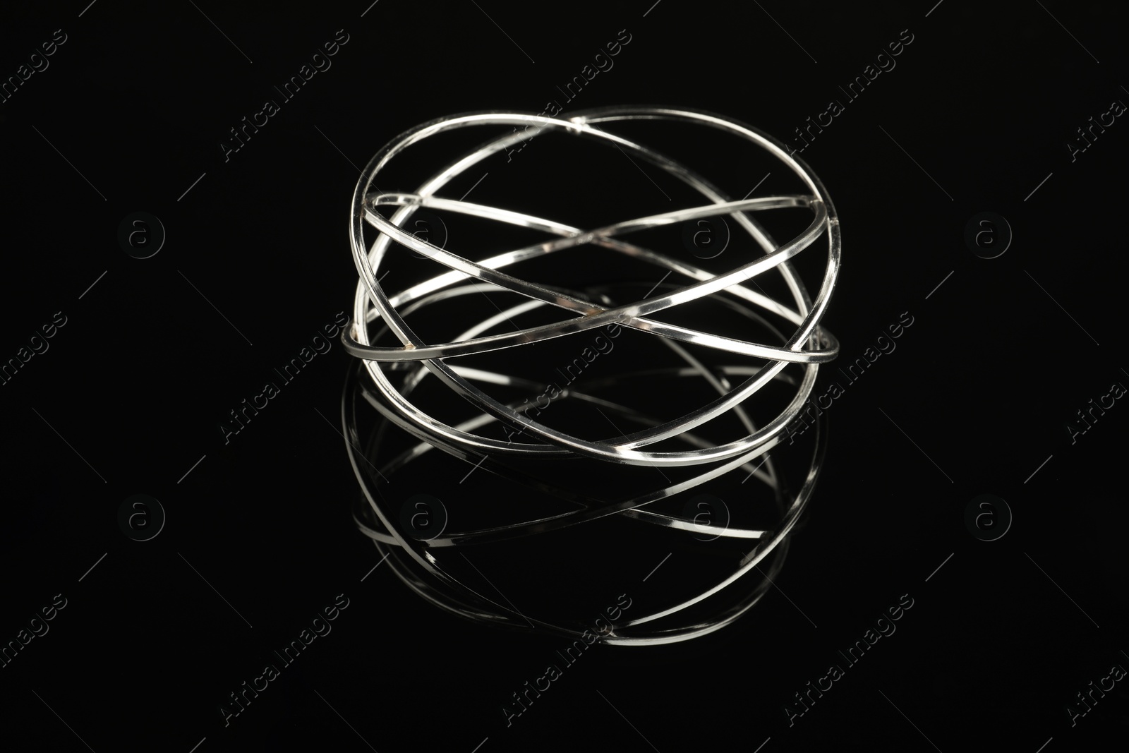 Photo of Beautiful bijouterie. Elegant bracelet on black mirror surface, closeup