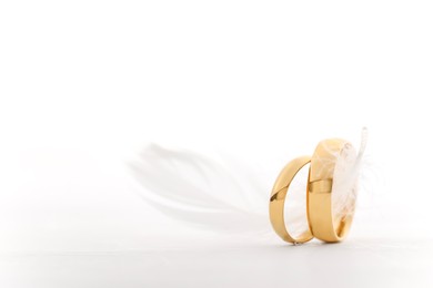 Photo of Beautiful golden wedding rings and feather on light background