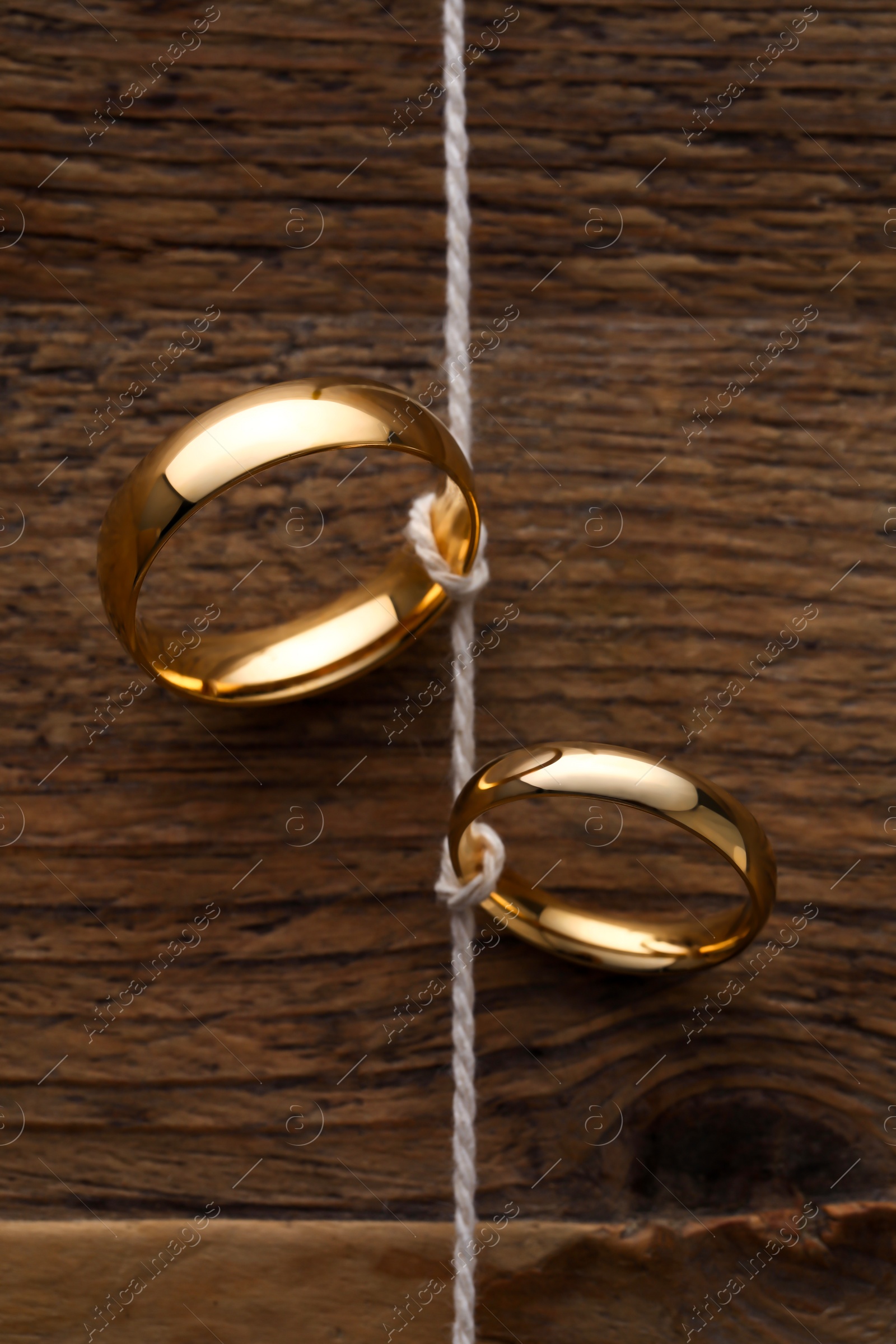 Photo of Beautiful golden wedding rings tied with thread on wooden background, above view