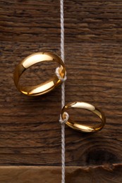 Photo of Beautiful golden wedding rings tied with thread on wooden background, above view