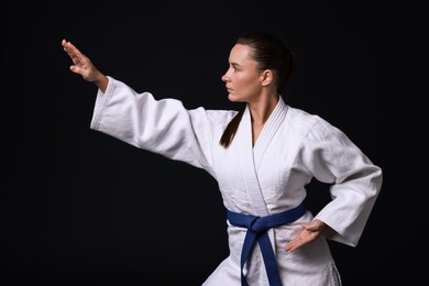 Photo of Young woman in kimono practicing karate on black background