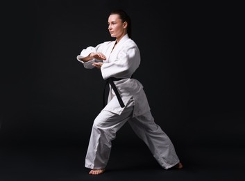 Photo of Young woman in kimono practicing karate on black background