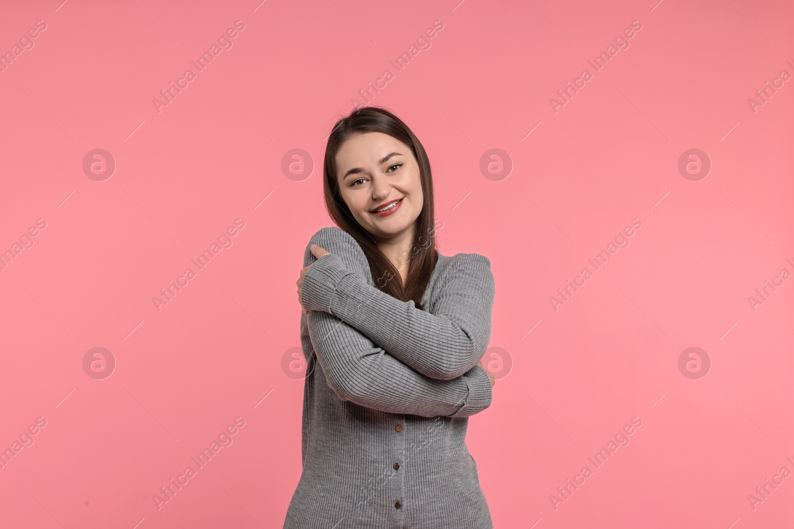 Photo of Beautiful young woman hugging herself on pink background