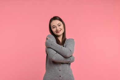 Photo of Beautiful young woman hugging herself on pink background