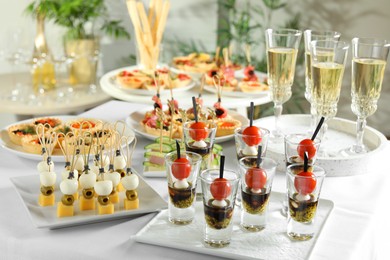 Photo of Many different tasty canapes and wine on white table