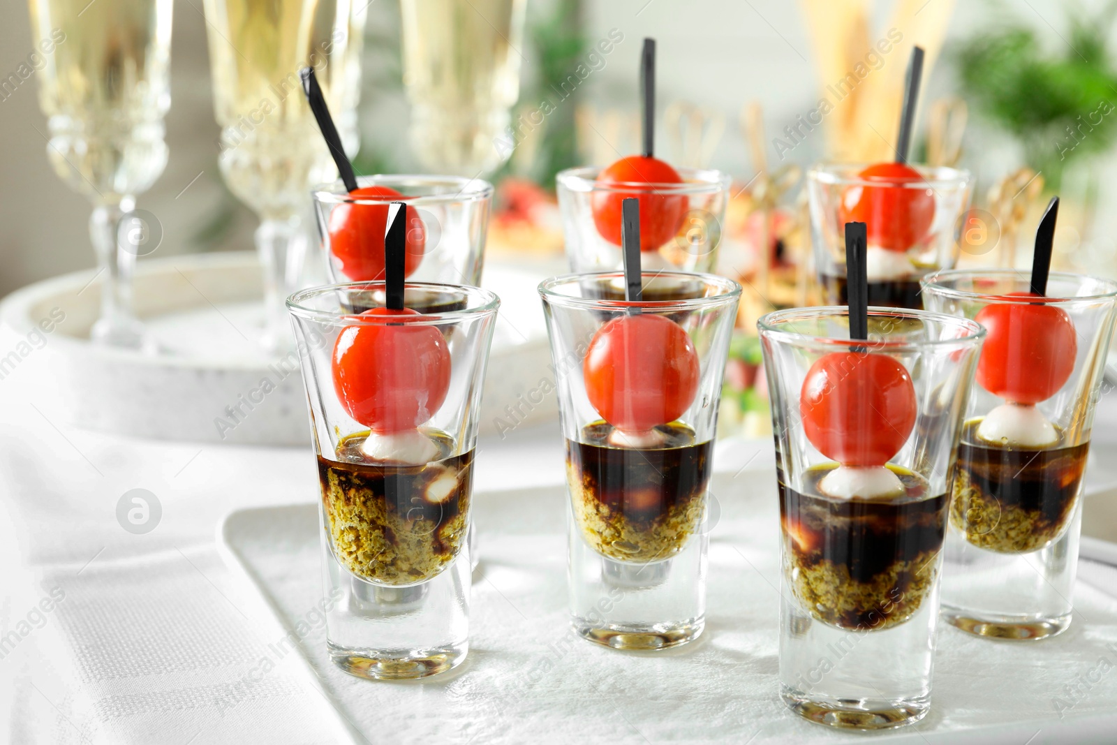 Photo of Tasty canapes with cherry tomatoes, mozzarella, balsamic vinegar and pesto sauce in shot glasses on white table, closeup