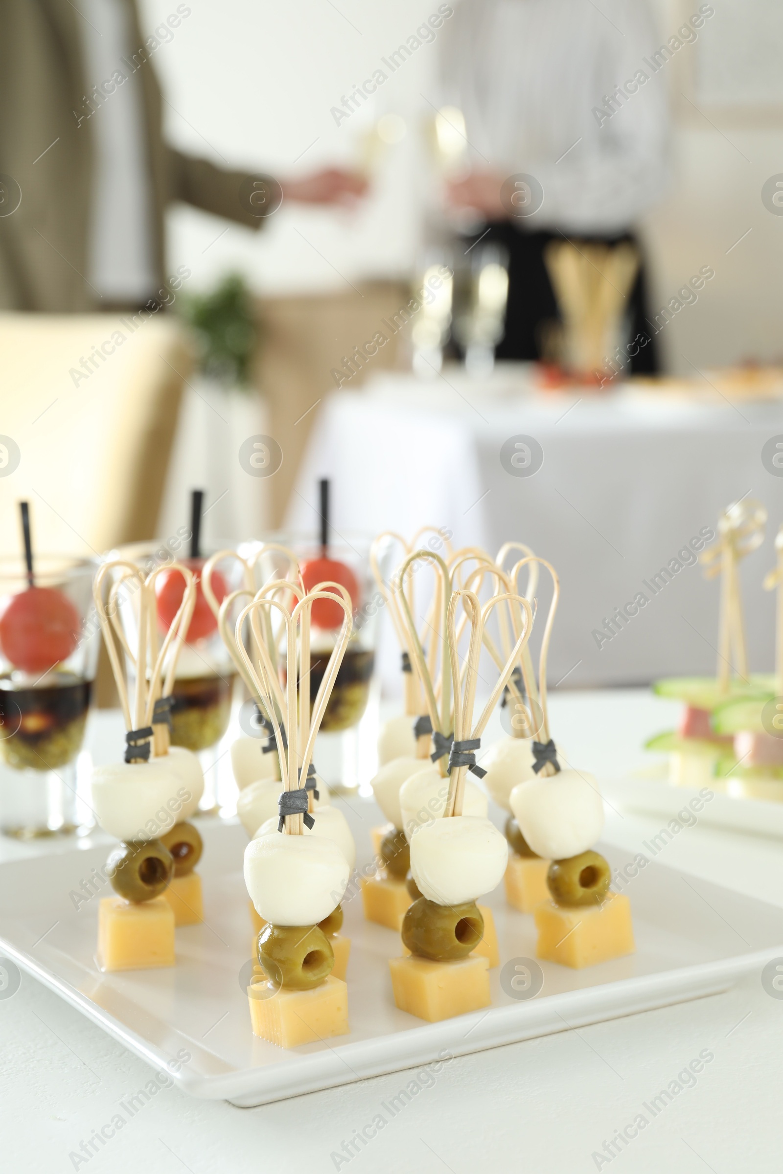 Photo of Many different tasty canapes on white table. People clinking glasses of wine indoors, closeup