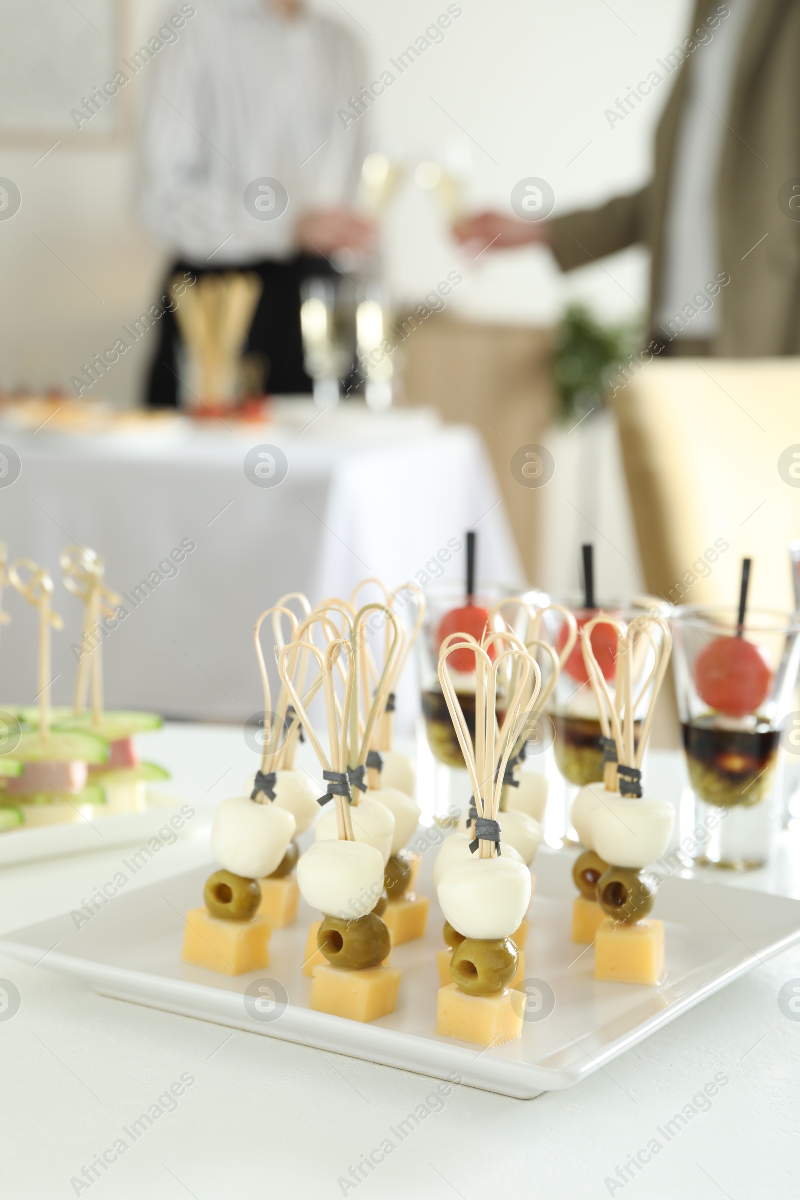 Photo of Many different tasty canapes on white table. People clinking glasses of wine indoors, closeup