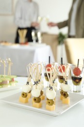 Photo of Many different tasty canapes on white table. People clinking glasses of wine indoors, closeup