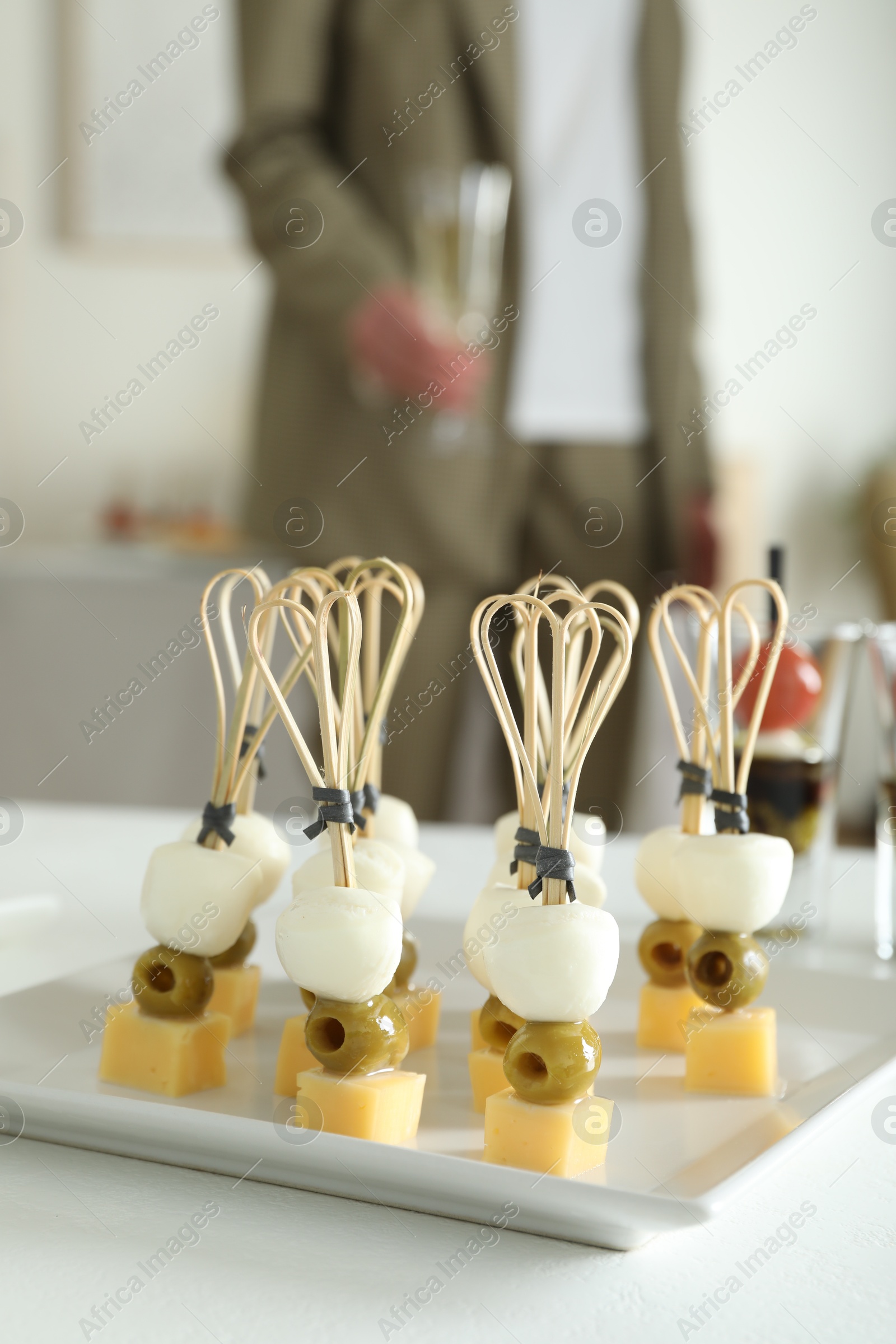 Photo of Many different tasty canapes on white table. Woman with glass of wine indoors, closeup