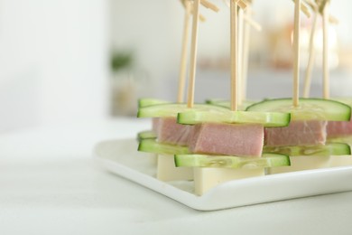 Photo of Tasty canapes with cucumbers, ham and cheese on white table, closeup. Space for text