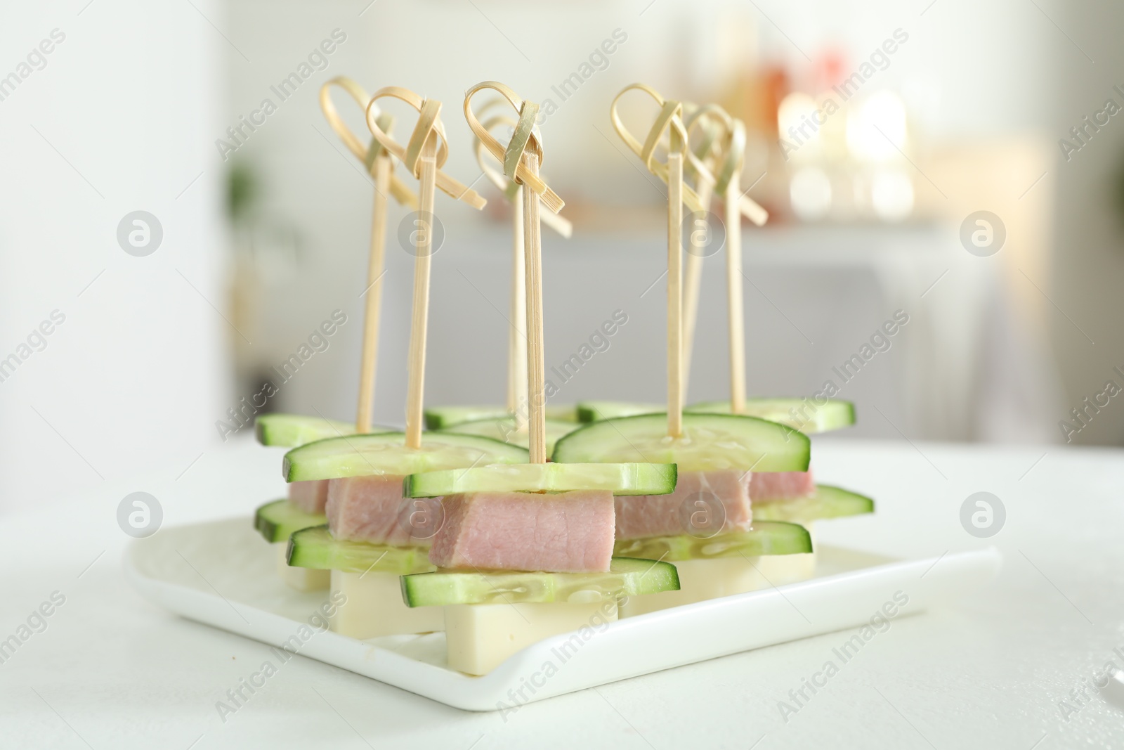 Photo of Tasty canapes with cucumbers, ham and cheese on white table