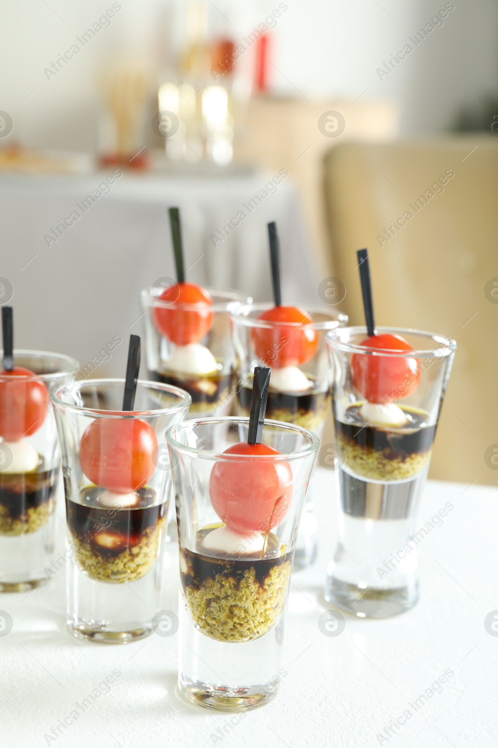 Photo of Tasty canapes with cherry tomatoes, mozzarella, balsamic vinegar and pesto sauce in shot glasses on white table