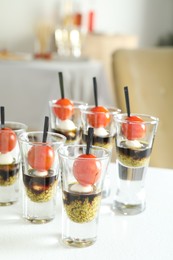 Photo of Tasty canapes with cherry tomatoes, mozzarella, balsamic vinegar and pesto sauce in shot glasses on white table