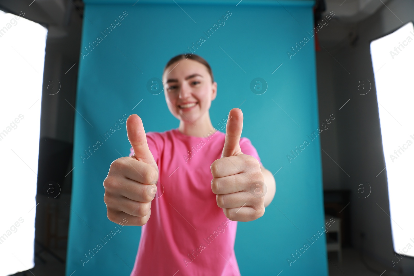 Photo of Smiling woman showing thumbs up on light blue background, selective focus