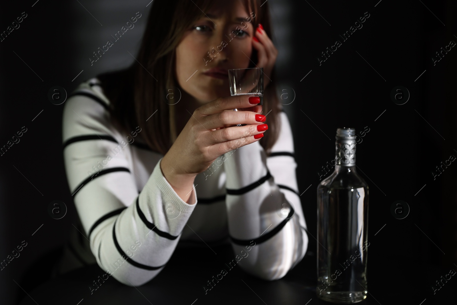 Photo of Alcohol addiction. Woman with shot glass of vodka and bottle at table indoors