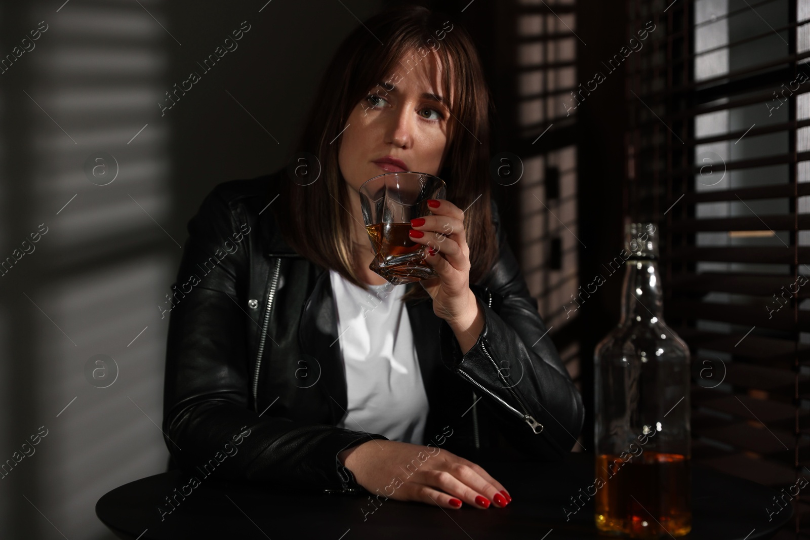 Photo of Alcohol addiction. Woman with glass of whiskey and bottle at table indoors