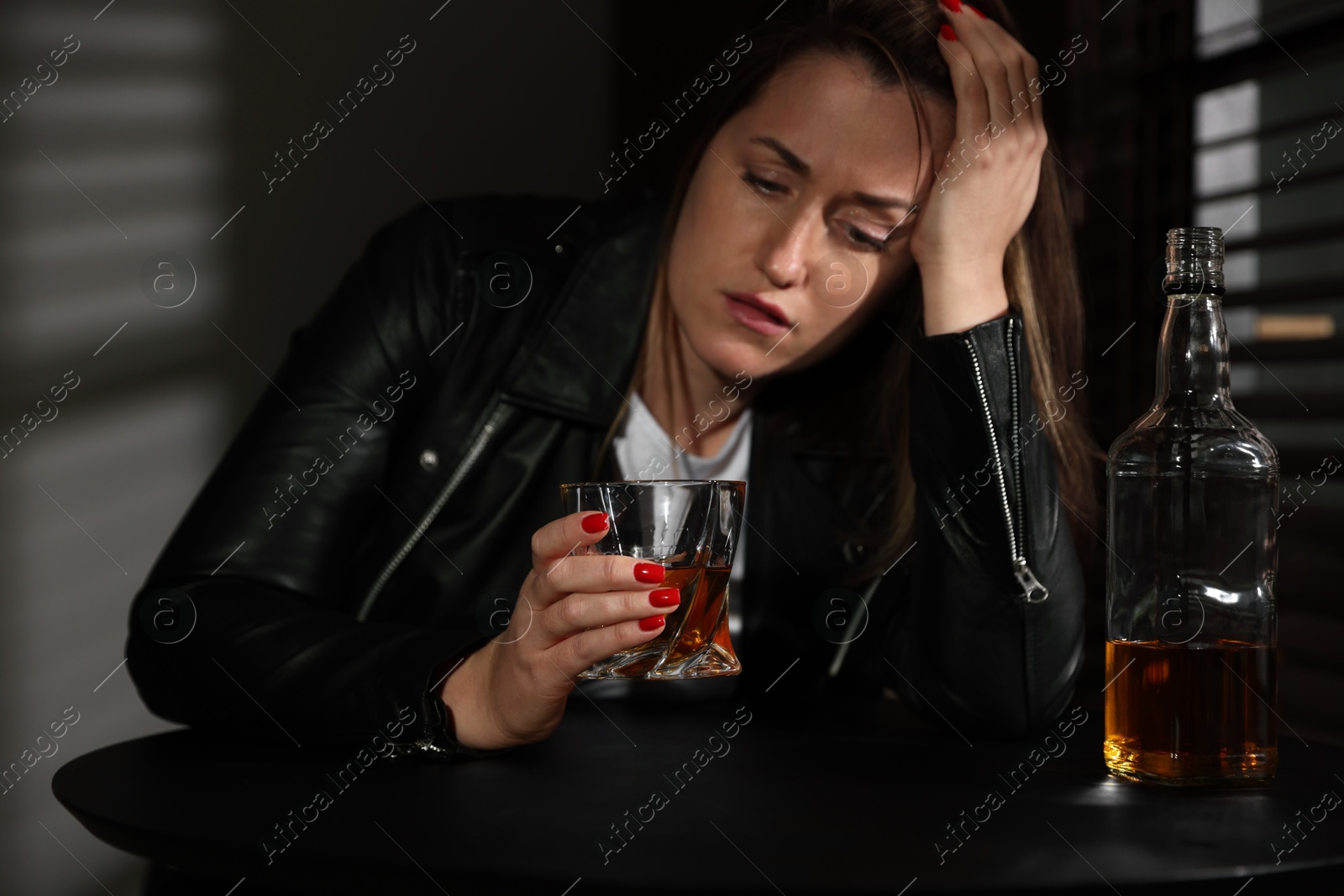 Photo of Alcohol addiction. Woman with glass of whiskey and bottle at table indoors