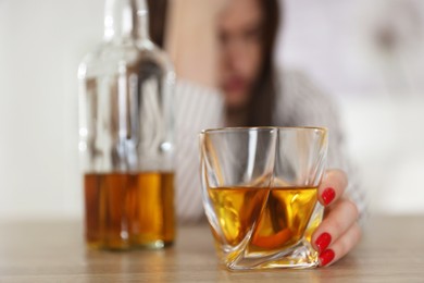 Alcohol addiction. Woman with glass of whiskey and bottle at wooden table indoors, selective focus