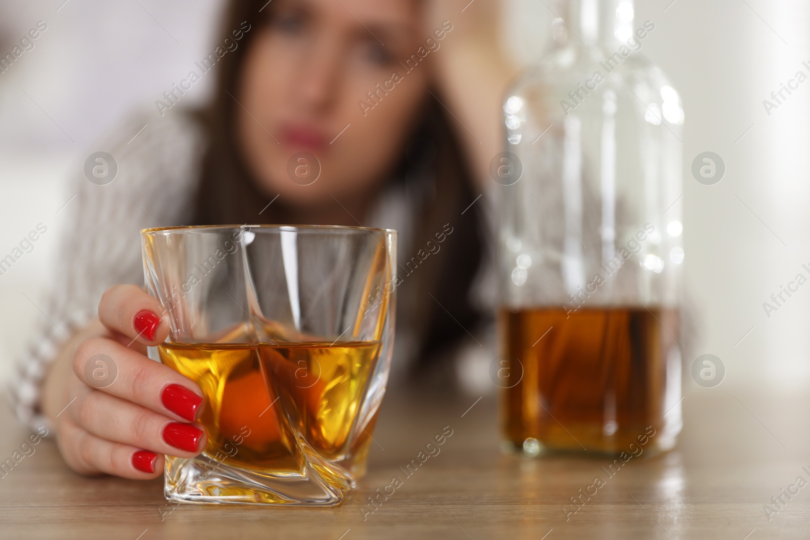 Photo of Alcohol addiction. Woman with glass of whiskey and bottle at wooden table indoors, selective focus