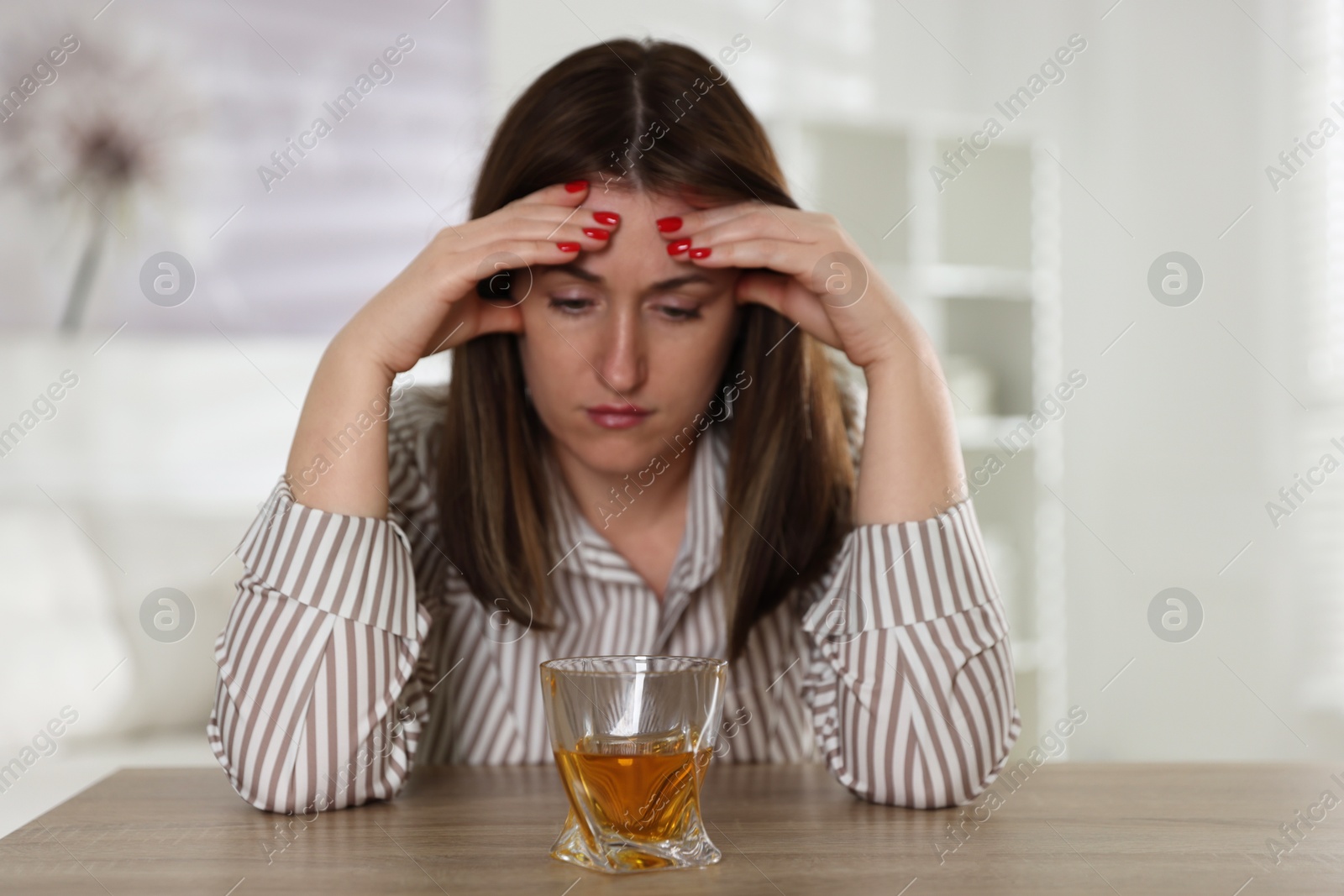 Photo of Alcohol addiction. Woman at wooden table with glass of whiskey indoors, selective focus