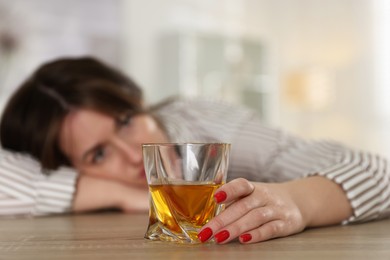 Alcohol addiction. Woman with glass of whiskey at wooden table indoors, selective focus