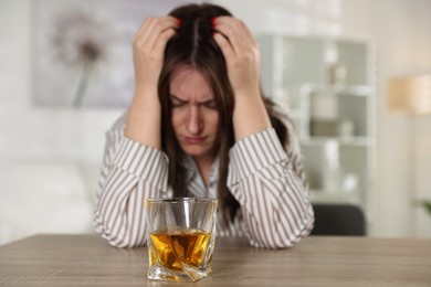 Alcohol addiction. Woman at wooden table indoors, focus on glass of whiskey