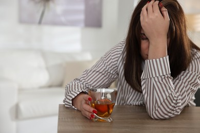 Alcohol addiction. Woman with glass of whiskey at wooden table indoors, space for text