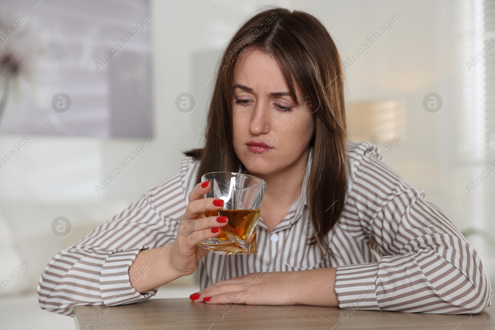 Photo of Alcohol addiction. Woman with glass of whiskey at wooden table indoors