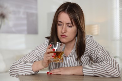 Alcohol addiction. Woman with glass of whiskey at wooden table indoors