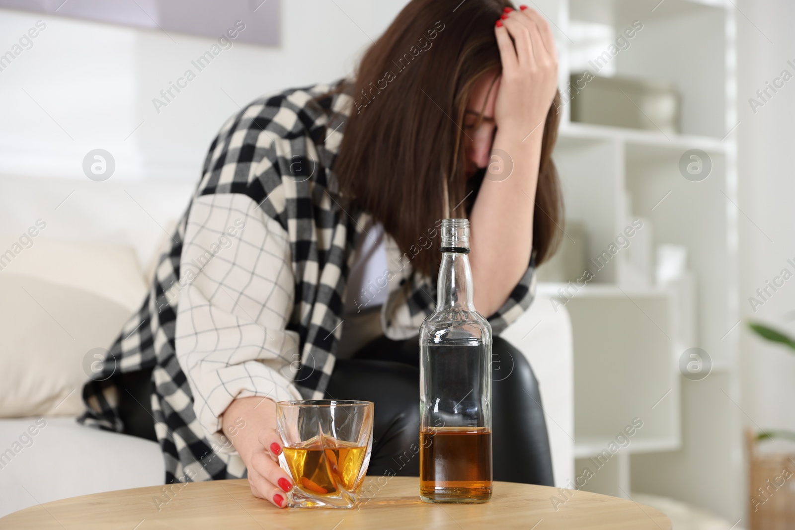 Photo of Alcohol addiction. Woman with glass of whiskey and bottle at home, space for text