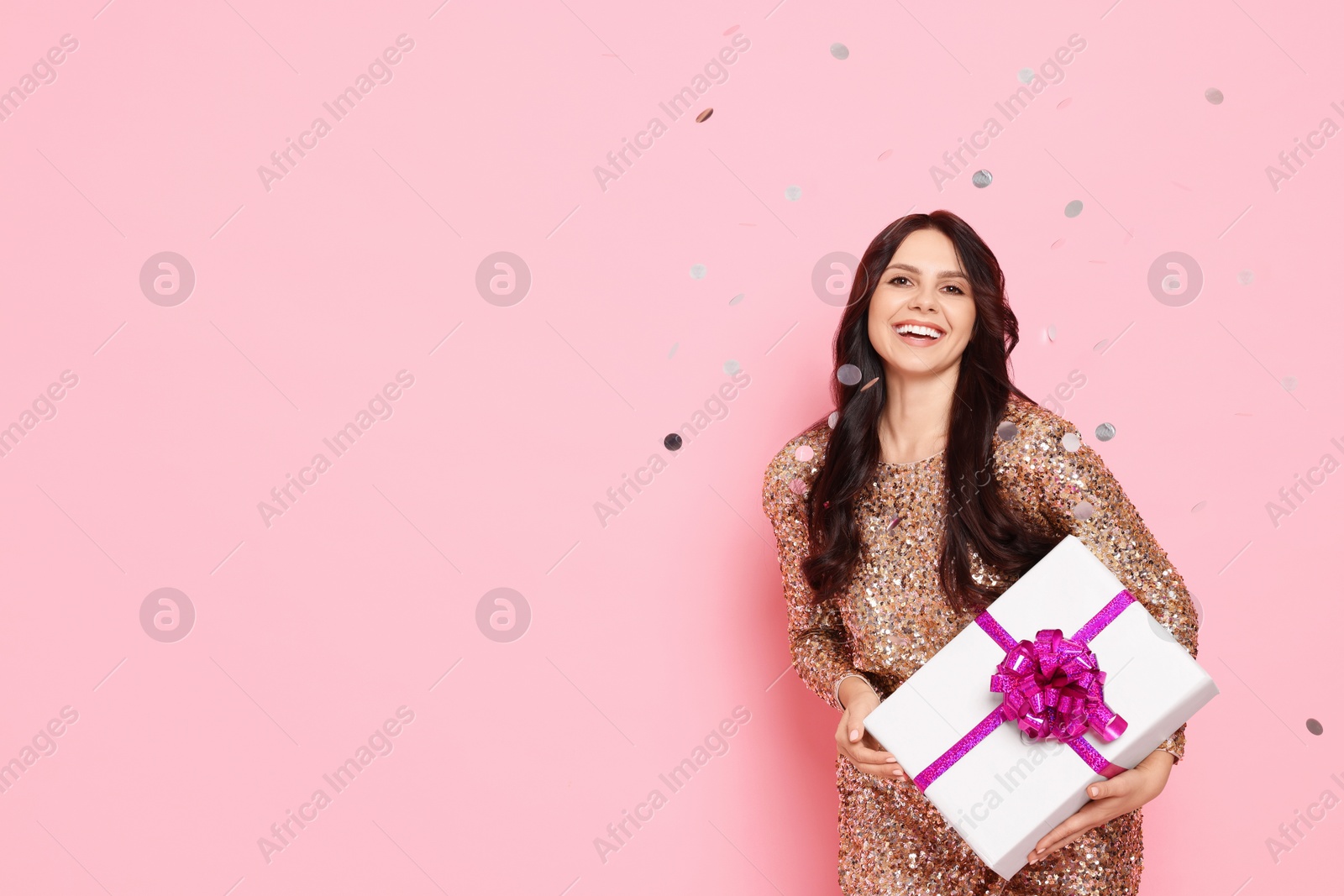 Photo of Happy woman with gift box and falling confetti on pink background, space for text. Surprise party