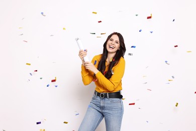 Photo of Happy woman blowing up confetti popper on white background. Surprise party