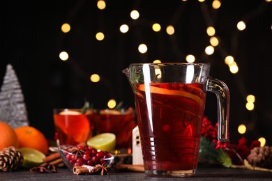 Photo of Tasty punch drink in glass jug and ingredients on dark table against blurred lights