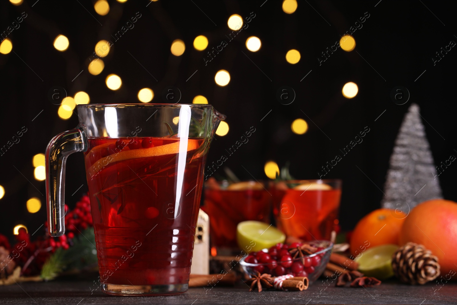 Photo of Tasty punch drink in glass jug and ingredients on dark table against blurred lights