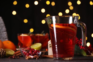 Photo of Tasty punch drink in glass jug and ingredients on dark table against blurred lights, closeup