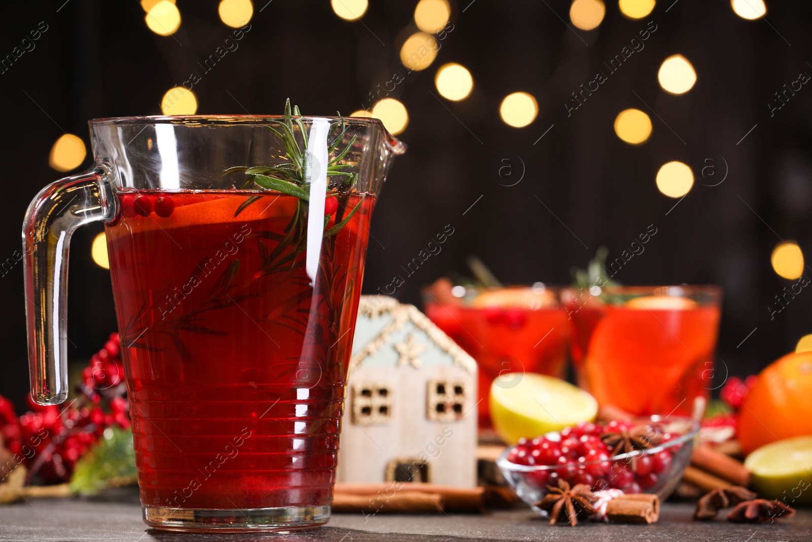 Photo of Tasty punch drink in glass jug and ingredients on dark table against blurred lights, closeup