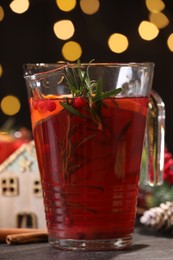 Photo of Tasty punch drink in glass jug on dark table against blurred lights, closeup